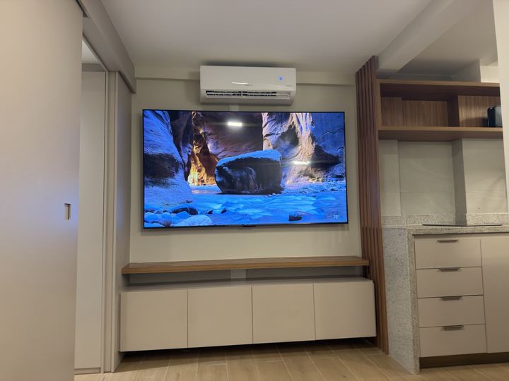 TV grande de parede com painel de madeira e armário