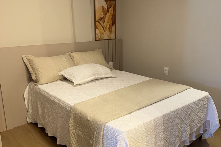 Cama de casal com manta bege e quadro na parede
