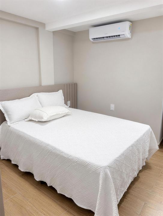 Cama arrumada com enxoval branco e ar-condicionado