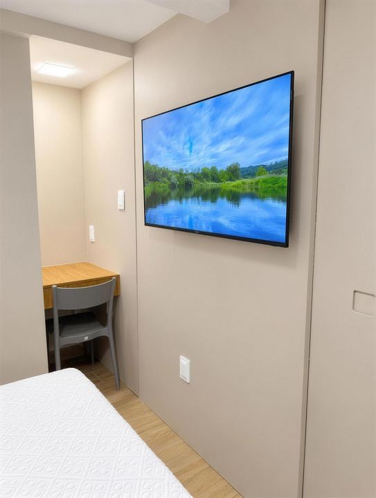 TV de parede e escrivaninha de madeira ao lado da cama