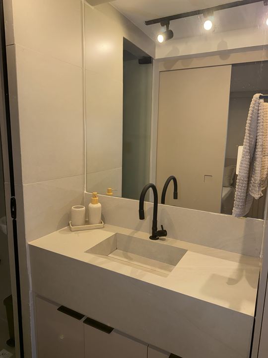 Banheiro com bancada branca, torneira preta e espelho