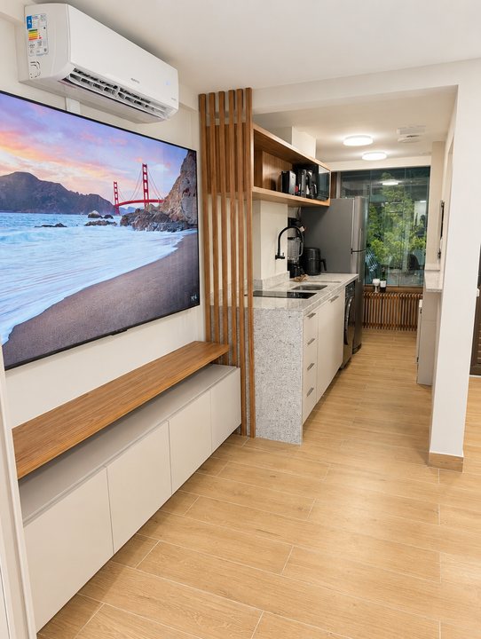 Sala com TV grande, painel de madeira e a cozinha ao fundo