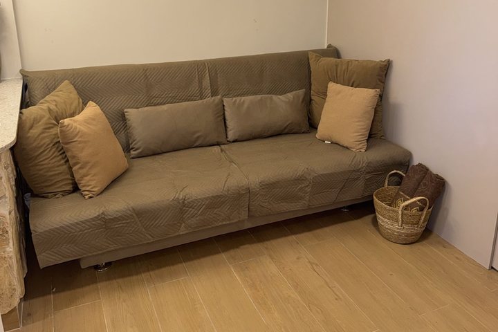 Sofá-cama bege com almofadas e cesto ao lado