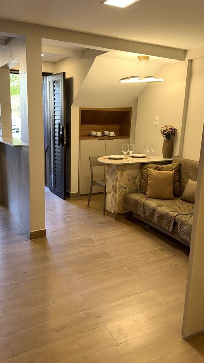 Entrada do apartamento com porta de madeira, mesa de pedra e sofá