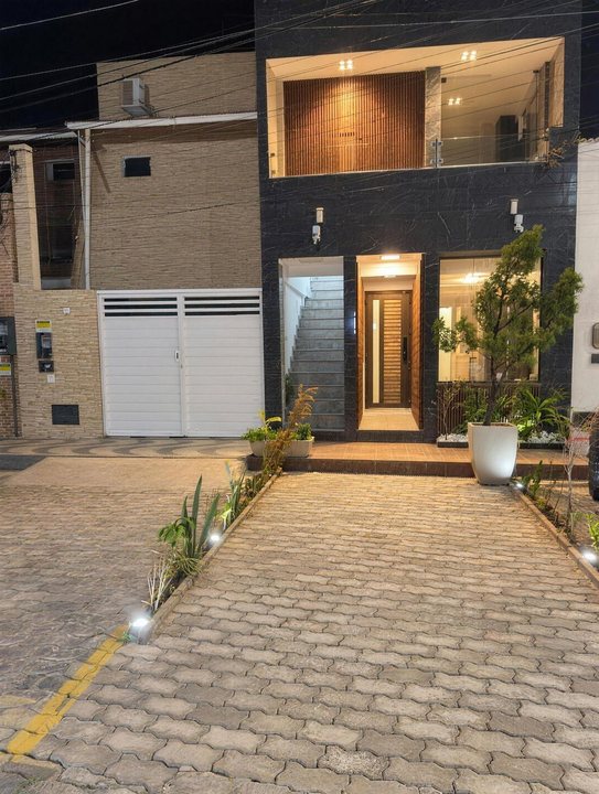 Fachada iluminada à noite, com pavimento de pedra